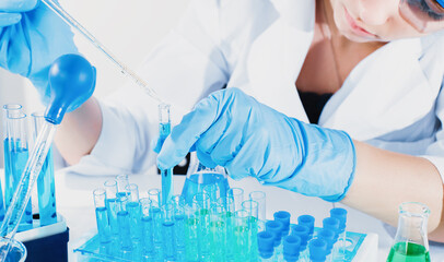 Professional female scientist in protective eyeglasses and mask making experiment with reagents in...