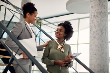 Happy black businesswoman talks to female mentor who leads her through office building. - obrazy, fototapety, plakaty