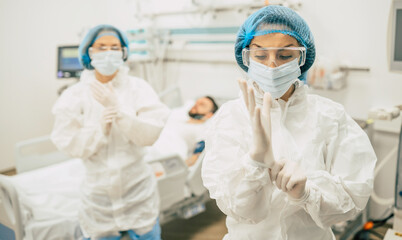 Naklejka premium Coronavirus covid-19 infected patient in a quarantine ward at the hospital with doctors in protective suits while they making disease treatment of him