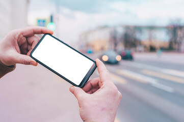 A man holds a mock-up of a smartphone with a white screen on the background of the road.