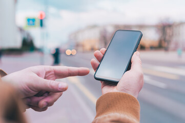 A man holds a mock-up of a smartphone on the background of the road.