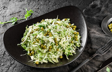 Fresh salad with cabbage, herbs and green peas served on a plate over a dark background, close up. Concept of healthy food, clean eating