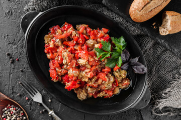 Delicious eggplant salad with pepper and tomatoes on large plate over dark background. Healthy vegan food, clean eating, top view