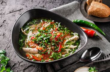 Traditional chicken soup with homemade noodles, vegetables, parsley in a bowl served with cream and chili peppers, dark background, close up view. Concept of healthy eating