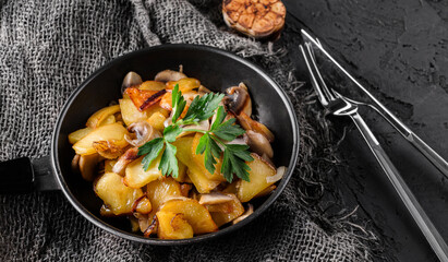 Homemade fried potatoes with mushrooms in a roasting pan with parsley, over a dark background, close up view