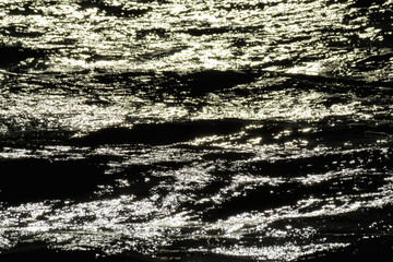 Obraz premium Sun glare on the water and ripples on the sea water. Black deep water with small waves close up.