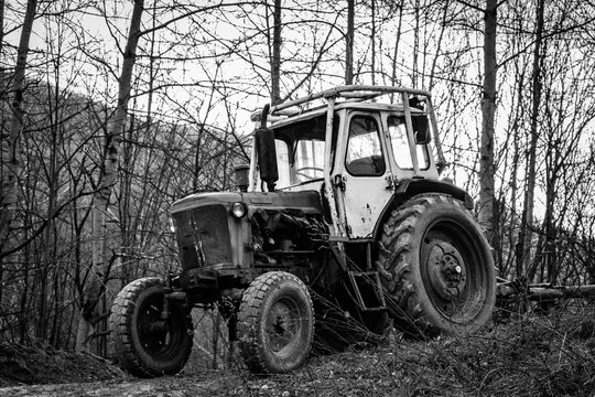 Old rusty wheeled tractor left in the winter leafless trees forest. Black and white moody picture