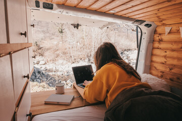 Vanlife - Young woman working on notebook in camping van surrounded by nature