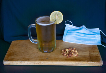 beer chopp with a lemon slice, peanuts and a mouth cover on a wooden surface and a black background