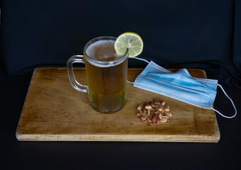 beer chopp with a lemon slice, peanuts and a mouth cover on a wooden surface and a black background