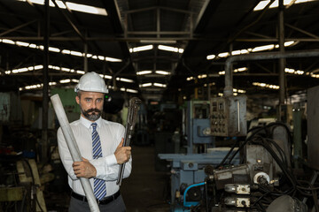 Naklejka na ściany i meble Factory manager with hard hat and blue print plan is checking his warehouse. Supervisor with beard in formal dress and hard hat checking his factory for any problems