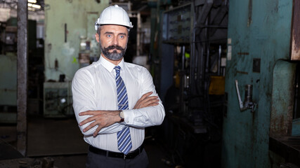 Factory manager with hard hat and blue print plan is checking his warehouse. Supervisor with beard  in formal dress and hard hat checking his factory for any problems