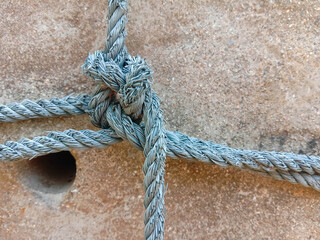 Old nylon ship ropes tied to knot bound around cement electrical post on ground flooring closeup.
