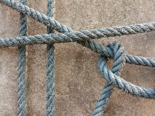 Old nylon ship ropes to knot bound around cement electrical post on ground flooring closeup.