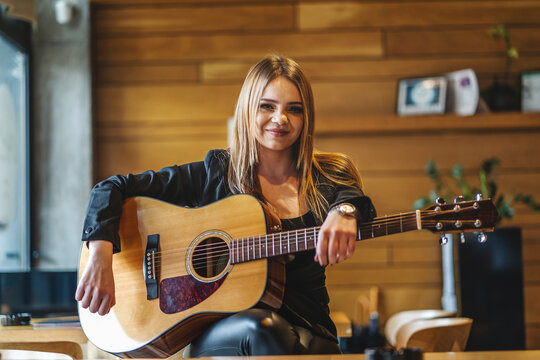 Front view portrait of adult caucasian woman sitting at empty cafe with guitar on her lap looking to the camera - female musician relaxed real people leisure concept