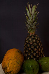 pineapple with papaya and avocado on dark background