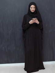 Young muslim businesswoman in traditional clothes or abaya using smartphone