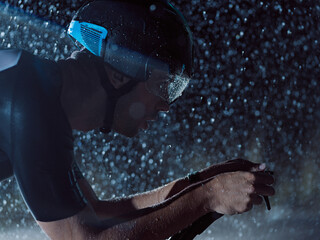 triathlon athlete riding bike on rainy night - obrazy, fototapety, plakaty