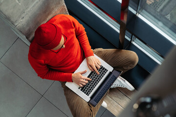 Above view of young freelancer man in glasses wear red hat and wool sweater sitting on bench next...