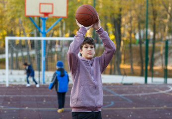 Cute Teenager with orange basketball ball plays basketball on street playground in spring summer. Hobby, active lifestyle, sports activity for kids.	