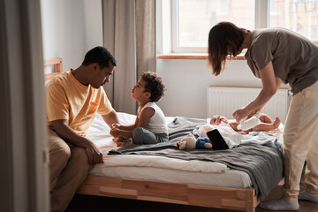 Father speaking with his multiracial son while his wife swaddles their child