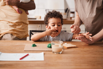 Boy sculpt from the plasticine while his mother giving breakfast for him