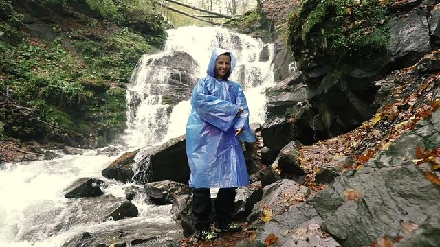 Raincoat. A woman in a raincoat is jumping against the background of a waterfall. Pylypets. Ukraine.