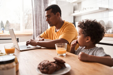 Obraz premium Man working at the laptop during the breakfast with his son