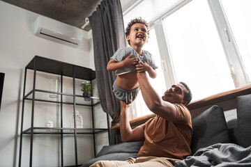 Obraz premium Dad playing with his son while holding him at the air at his hands