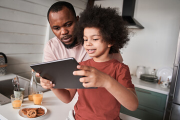 Father looking at the tablet while his son showing funny applications to him