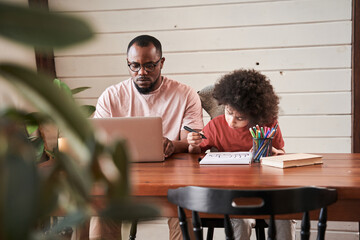 Boy drawing diligently near his father at the table