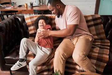 Father tickling and playing with his son laying at the sofa