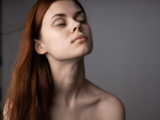 Portrait of a romantic red-haired woman with bare shoulders on a gray background