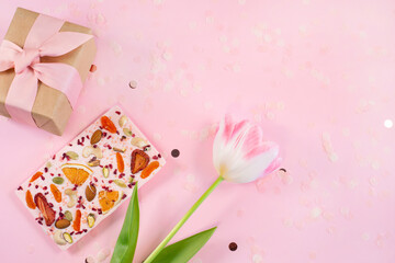 View of gift box, flower and Handmade pink chocolate bar with dried fruits and nuts on a fastive Pink Background