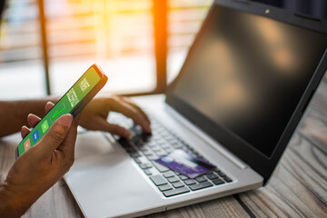 Fototapeta premium Men use smartphones to shop online. Businessmen transfer money via the Internet. A man's hand holds a smartphone to payment. Business people use laptops on a desk. Selective focus. Blurred background.
