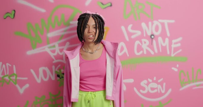 Youth subculture and urban lifestyle concept. Cool funky female teenager with dreadlocks raises index finger has self confident expression dressed in stylish clothes poses against graffiti wall