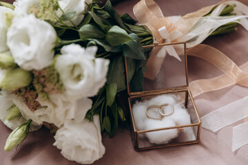 wedding gold rings in a glass box lie next to a wedding bouquet  with austom. aesthetics and details of the wedding