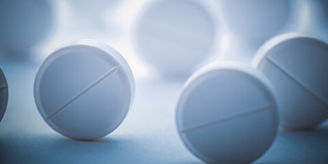A pile of white pills scattered on a white background with blue tinting. Selective focus.
