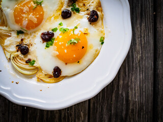 Continental breakfast - sunny side up eggs with onion and parmesan on wooden background