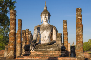 Sculpture of a seated Buddha on the ruins of a Bujjist temple on a sunny evening. Sukhothai,...