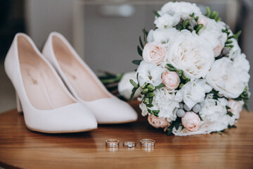The wedding bouquet, the bride's shoes and the wedding rings lie on the table. aesthetics and details of the wedding - 421981878