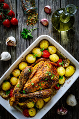 Whole roast chicken with vegetables on wooden table
