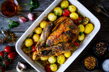 Whole roast chicken with vegetables on wooden table
