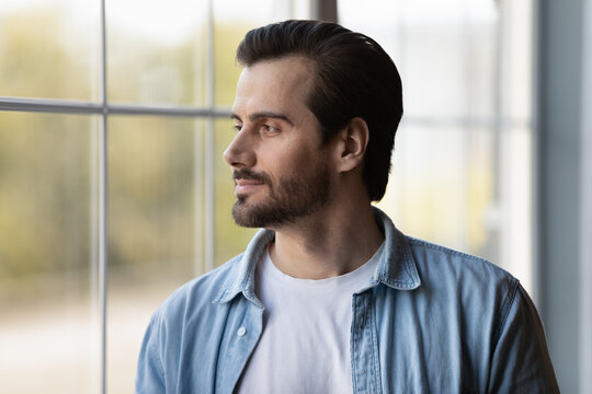 Pensive Young 20s Caucasian Man Look In Window Distance Thinking Pondering Of Future Opportunities. Thoughtful Millennial Male Dream Or Imagine New Possibilities. Visualization Concept.