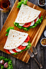 Italian piada wraps - piadina stuffed with fresh lettuce  mozzarella and sliced tomatoes on wooden...