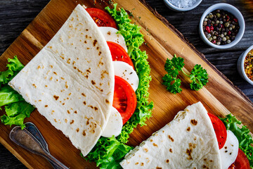 Italian piada wraps - piadina stuffed with fresh lettuce  mozzarella and sliced tomatoes on wooden...