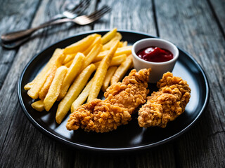 Fried breaded chicken nuggets with French fries and ketchup on wooden table
