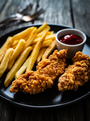 Fried breaded chicken nuggets with French fries and ketchup on wooden table
