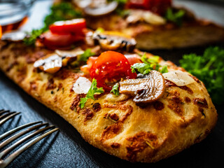 Focaccia - roasted mozzarella sandwiches with white mushrooms, tomatoes and prosciutto ham on black stone plate 