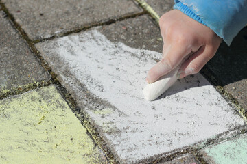Kind malt mit Malkreide auf Pflastersteinen